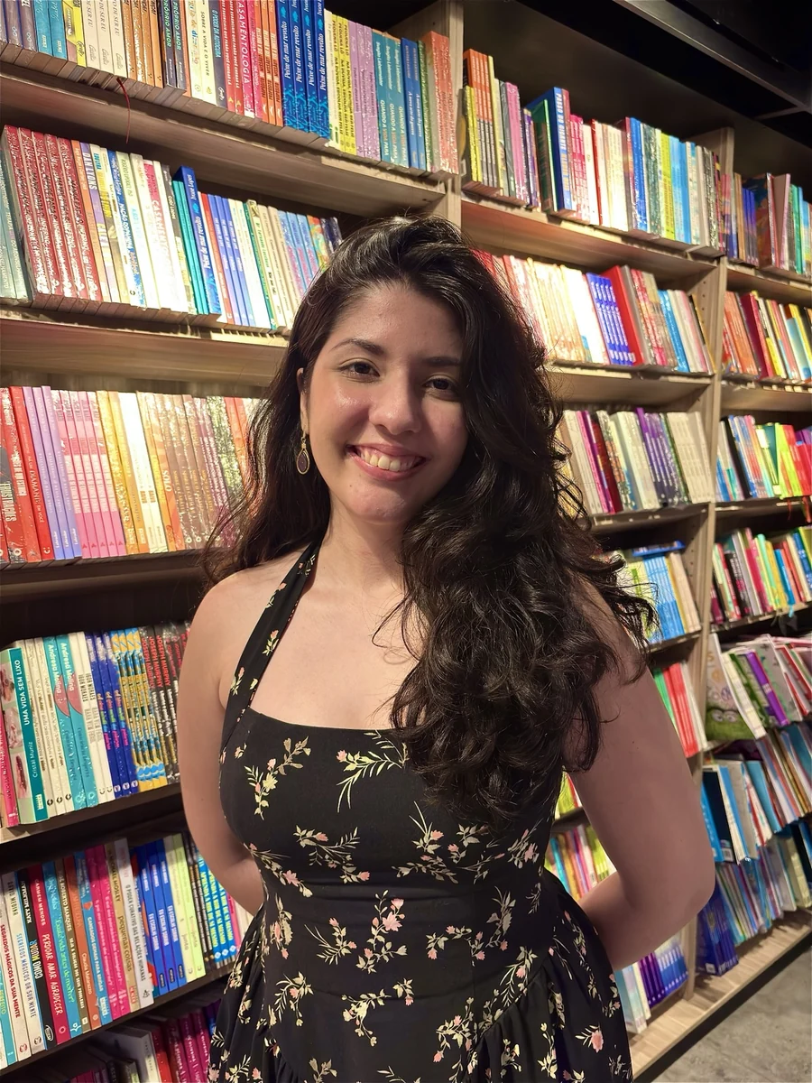 Julie sorrindo em frente a uma estante de livros coloridos